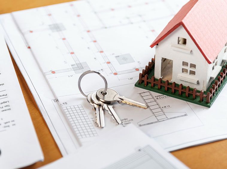 Un juego de llaves de casa y una pequeña maqueta de casa con tejado rojo se sitúan sobre planos y documentos arquitectónicos, simbolizando la propiedad inmobiliaria, la compra de casas o la planificación de la construcción.